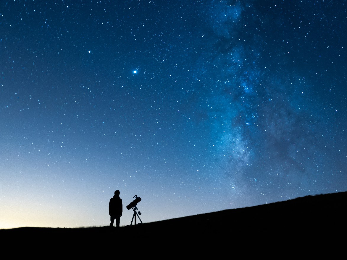 Silhouette of an astronomer beside a telescope under a starry night sky with the Milky Way